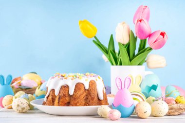 Geleneksel Paskalya pastası şekerleme ve şekerle süslenmiş, şenlikli ruh dekorasyonu ve çiçek buketiyle süslenmiş. Paskalya kutlamaları pastel renkli Paskalya yumurtaları ve tavşan tavşanlarıyla dolu tatil masası.