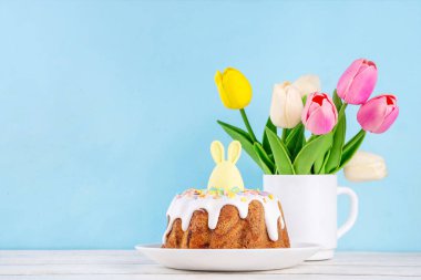 Geleneksel Paskalya pastası şekerleme ve şekerle süslenmiş, şenlikli ruh dekorasyonu ve çiçek buketiyle süslenmiş. Paskalya kutlamaları pastel renkli Paskalya yumurtaları ve tavşan tavşanlarıyla dolu tatil masası.