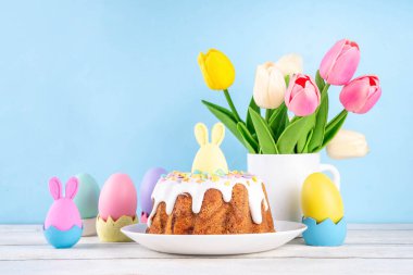 Geleneksel Paskalya pastası şekerleme ve şekerle süslenmiş, şenlikli ruh dekorasyonu ve çiçek buketiyle süslenmiş. Paskalya kutlamaları pastel renkli Paskalya yumurtaları ve tavşan tavşanlarıyla dolu tatil masası.