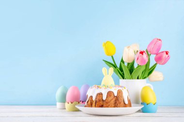 Geleneksel Paskalya pastası şekerleme ve şekerle süslenmiş, şenlikli ruh dekorasyonu ve çiçek buketiyle süslenmiş. Paskalya kutlamaları pastel renkli Paskalya yumurtaları ve tavşan tavşanlarıyla dolu tatil masası.