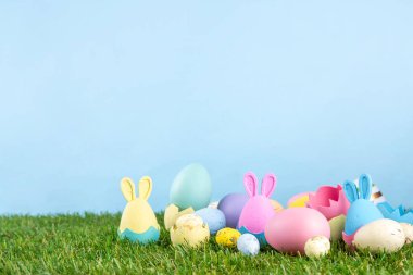 Paskalya geleneği, Paskalya yumurtası avı hazırlığı, çocuk partisi geçmişine davetiye. Renkli dekorasyon tavşanları ve çimlerde Paskalya yumurtaları ve mavi arkaplan, boşluğu kopyala