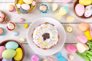 Geleneksel Paskalya pastası şekerleme ve şekerle süslenmiş, şenlikli ruh dekorasyonu ve çiçek buketiyle süslenmiş. Paskalya kutlamaları pastel renkli Paskalya yumurtaları ve tavşan tavşanlarıyla dolu tatil masası.