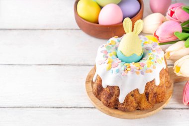 Geleneksel Paskalya pastası şekerleme ve şekerle süslenmiş, şenlikli ruh dekorasyonu ve çiçek buketiyle süslenmiş. Paskalya kutlamaları pastel renkli Paskalya yumurtaları ve tavşan tavşanlarıyla dolu tatil masası.