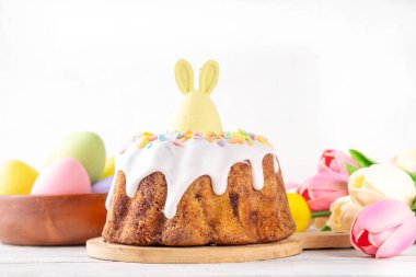 Geleneksel Paskalya pastası şekerleme ve şekerle süslenmiş, şenlikli ruh dekorasyonu ve çiçek buketiyle süslenmiş. Paskalya kutlamaları pastel renkli Paskalya yumurtaları ve tavşan tavşanlarıyla dolu tatil masası.