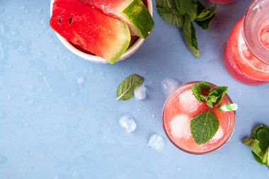 Ev yapımı karpuz limonatası, ferahlatıcı tatlı yaz içeceği, naneli buzlu karpuz suyu ve çizgili kamış, açık mavi ve ahşap arka plan, kopyalama alanı. 