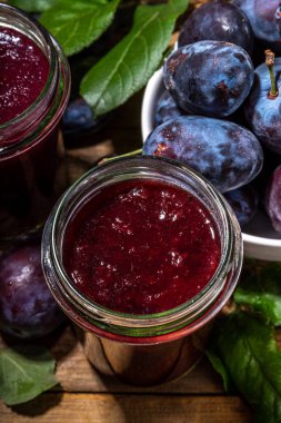 Red blue plum jam in small jar. Homemade autumn plum jam with fresh fruits. Fall preparations and canning on white table background copy space