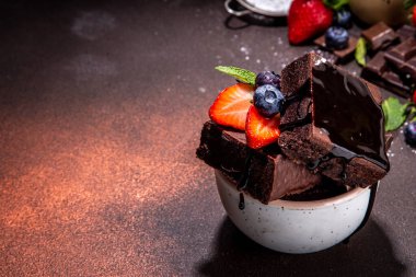 Böğürtlenli siyah çikolatalı kek. Üzerine çikolata sosu serpiştirilmiş ev yapımı kek kurabiyeleri ve koyu arkaplanda taze çilek, yabanmersini, fotokopi alanı.