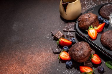 Çilekli çikolatalı kek. Kakao soslu ev yapımı çikolatalı kek tepsisi, şeker tozu ve taze çilek, yabanmersini, koyu kahverengi arka plan fotokopi alanı.