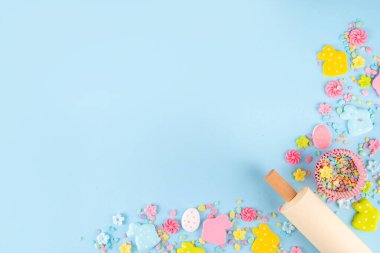 Paskalya arkaplanda şeker serpiştirme, paskalya tavşanı, paskalya yumurtası ve bahar çiçeği süslemesi, merdane ve fırın aksesuarları, açık mavi arka plan üst görünüm kopya alanı