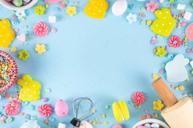 Paskalya arkaplanda şeker serpiştirme, paskalya tavşanı, paskalya yumurtası ve bahar çiçeği süslemesi, merdane ve fırın aksesuarları, açık mavi arka plan üst görünüm kopya alanı