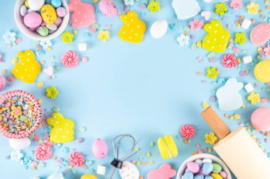 Paskalya arkaplanda şeker serpiştirme, paskalya tavşanı, paskalya yumurtası ve bahar çiçeği süslemesi, merdane ve fırın aksesuarları, açık mavi arka plan üst görünüm kopya alanı
