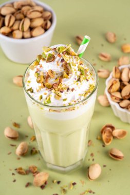 Pistachio milkshake, sağlıklı diyet protein kokteyli, sütsüz kremalı vejetaryen fıstıklı süt, çırpılmış bitkisel krema, fındık serpiştirilmiş, açık yeşil arka plan.