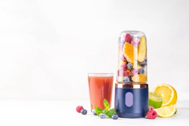 Portatif blender, meyve suyu, meyve suyu ve milkshake 'te sağlıklı meyve suyu ve meyve suyu. Şeffaf blender bardakta meyveler ve masa arkasında taze meyve suyu bardakları.