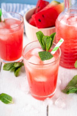 Ev yapımı karpuz limonatası, ferahlatıcı tatlı yaz içeceği, naneli buzlu karpuz suyu ve çizgili kamış, açık mavi ve ahşap arka plan, kopyalama alanı. 