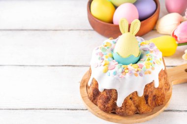 Geleneksel Paskalya pastası şekerleme ve şekerle süslenmiş, şenlikli ruh dekorasyonu ve çiçek buketiyle süslenmiş. Paskalya kutlamaları pastel renkli Paskalya yumurtaları ve tavşan tavşanlarıyla dolu tatil masası.