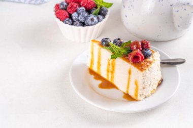 Geleneksel New York peynirli kek dilimleri tabakta, taze böğürtlenler beyaz mutfak masasında