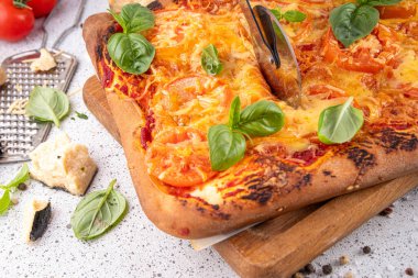 Domates ve fesleğenli ev yapımı margarita pizza, malzemeler ve arka planda beyaz mutfak masasında zeytinyağı.