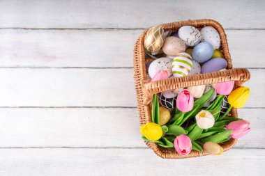 Paskalya boyalı geleneksel yumurtalar, lale çiçekleri sepetin içinde beyaz ahşap arka planda. Paskalya tebrik kartı, yumurta avı aile eğlence festivali davetiyesi arka plan fotokopi alanı