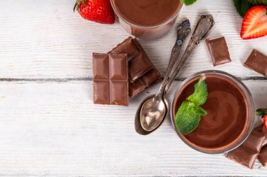 Ev yapımı çikolatalı puding, seramik porsiyonlu kase içinde mutfak masasında, taze çilek, nane ve çikolata dilimleri ile.