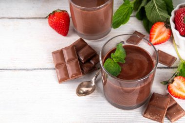 Ev yapımı çikolatalı puding, seramik porsiyonlu kase içinde mutfak masasında, taze çilek, nane ve çikolata dilimleri ile.