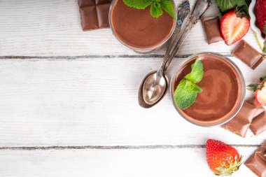 Ev yapımı çikolatalı puding, seramik porsiyonlu kase içinde mutfak masasında, taze çilek, nane ve çikolata dilimleri ile.