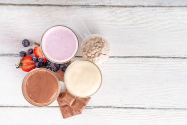 Hızlı ve basit protein pudingi. Sağlıklı yaz soğuk tatlısı. Üç bardak vanilyalı, çikolatalı ve çilekli puding, çikolata dilimleri, taze çilek, yabanmersini, protein tozu