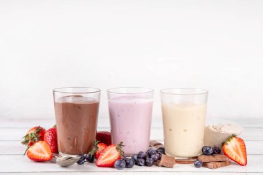 Hızlı ve basit protein pudingi. Sağlıklı yaz soğuk tatlısı. Üç bardak vanilyalı, çikolatalı ve çilekli puding, çikolata dilimleri, taze çilek, yabanmersini, protein tozu