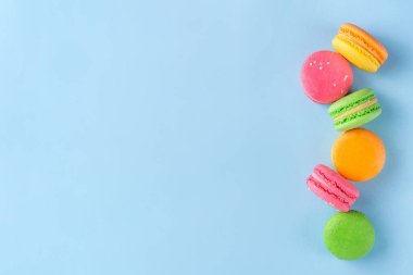 Taze meyveli, parlak ve renkli badem kurabiyesi tatlısı. Açık mavi arka planda pembe, turuncu, sarı ve şam fıstıklı yeşil, lezzetli makaron kurabiyeleri kopyalama alanı