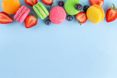 Taze meyveli, parlak ve renkli badem kurabiyesi tatlısı. Açık mavi arka planda pembe, turuncu, sarı ve şam fıstıklı yeşil, lezzetli makaron kurabiyeleri kopyalama alanı