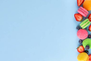 Taze meyveli, parlak ve renkli badem kurabiyesi tatlısı. Açık mavi arka planda pembe, turuncu, sarı ve şam fıstıklı yeşil, lezzetli makaron kurabiyeleri kopyalama alanı