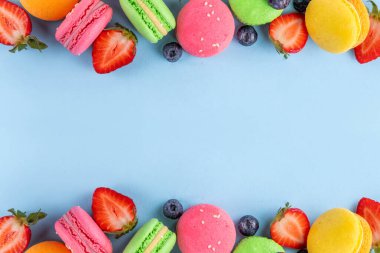 Taze meyveli, parlak ve renkli badem kurabiyesi tatlısı. Açık mavi arka planda pembe, turuncu, sarı ve şam fıstıklı yeşil, lezzetli makaron kurabiyeleri kopyalama alanı