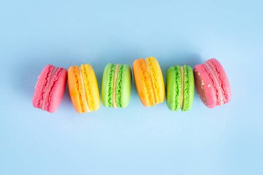 Taze meyveli, parlak ve renkli badem kurabiyesi tatlısı. Açık mavi arka planda pembe, turuncu, sarı ve şam fıstıklı yeşil, lezzetli makaron kurabiyeleri kopyalama alanı