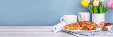 Anneler Günü kahvaltı arka planında kruvasan, çilek, çikolata, kahve fincanı, bir buket lale çiçeği, sürpriz ve hediye olarak, annem için tebrik kartı..
