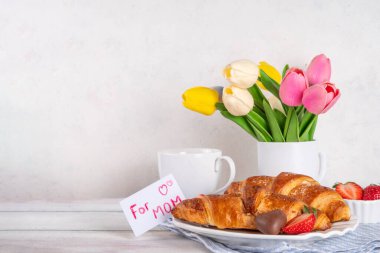 Anneler Günü kahvaltı arka planında kruvasan, çilek, çikolata, kahve fincanı, bir buket lale çiçeği, sürpriz ve hediye olarak, annem için tebrik kartı..