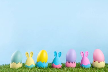 Paskalya geleneği, Paskalya yumurtası avı hazırlığı, çocuk partisi geçmişine davetiye. Renkli dekorasyon tavşanları ve çimlerde Paskalya yumurtaları ve mavi arkaplan, boşluğu kopyala