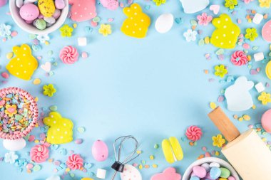 Paskalya arkaplanda şeker serpiştirme, paskalya tavşanı, paskalya yumurtası ve bahar çiçeği süslemesi, merdane ve fırın aksesuarları, açık mavi arka plan üst görünüm kopya alanı