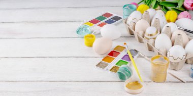 Aile gelenekleri, Paskalya hazırlıkları. Bahar çiçeği laleleri, dekoratif Paskalya yumurtaları boyalı, fırçalı, aksesuarlı beyaz ahşap arka planda yumurta çizip boyamak için aksesuarlar.