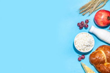 Yahudi bayramının sembolleri olan mutlu Shavuot tebrik kartı - nar, üzüm, elma, tatlı challah ekmeği, buğday filizi, süt, peynir, süzme peynir, açık mavi zemin