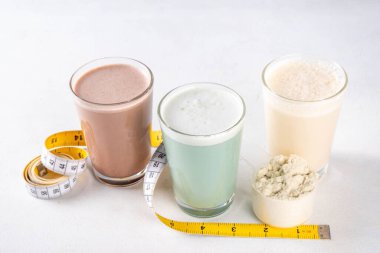 Protein tozu kepçesi ve mezurayla protein kokteyllerinin çeşitli çeşitleri. Protein, kilo vermek için sallanıyor, her gün protein hedefleri, spor ve spor, sağlıklı yaşam tarzı.