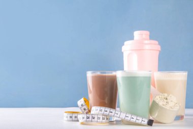 Protein tozu kepçesi ve mezurayla protein kokteyllerinin çeşitli çeşitleri. Protein, kilo vermek için sallanıyor, her gün protein hedefleri, spor ve spor, sağlıklı yaşam tarzı.
