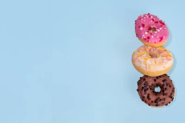 Açık mavi arka planda tatlı renkli şekerli donutlar. Üç lezzetli çörek - çikolata, vanilya, çilek pembesi, fotokopi alanı