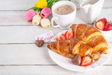 Anneler Günü kahvaltı arka planında kruvasan, çilek, çikolata, kahve fincanı, bir buket lale çiçeği, sürpriz ve hediye olarak annem için 