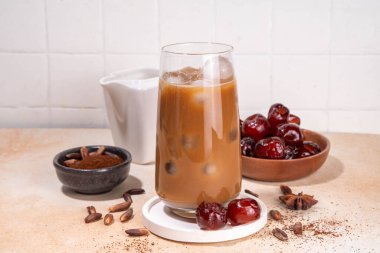 Sağlıklı organik hurma tohumu kahvesi, rendelenmiş hurma tohumlarıyla yapılmış buzlu kahve fincanı, bej arka planda tüm hurma meyveleri ve tohumlarla birlikte. Alternatif sıcak kahve.