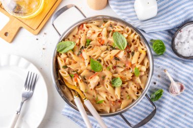 Son moda viral benimle tavuk makarnası evlen. Bir tencere yumuşak makarna ve kremalı ve peynirli sulu tavuk parçaları, sarımsaklı güneşte kurutulmuş domates sosu, nükteli fesleğen yaprağı, tabak ve demlikte.