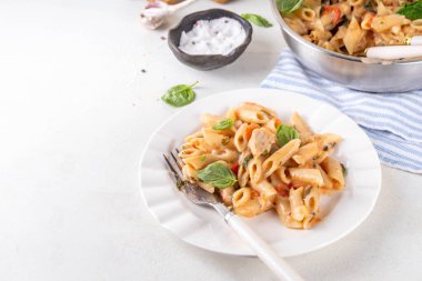 Son moda viral benimle tavuk makarnası evlen. Bir tencere yumuşak makarna ve kremalı ve peynirli sulu tavuk parçaları, sarımsaklı güneşte kurutulmuş domates sosu, nükteli fesleğen yaprağı, tabak ve demlikte.