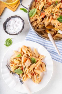 Son moda viral benimle tavuk makarnası evlen. Bir tencere yumuşak makarna ve kremalı ve peynirli sulu tavuk parçaları, sarımsaklı güneşte kurutulmuş domates sosu, nükteli fesleğen yaprağı, tabak ve demlikte.