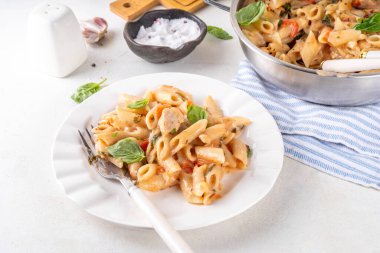 Son moda viral benimle tavuk makarnası evlen. Bir tencere yumuşak makarna ve kremalı ve peynirli sulu tavuk parçaları, sarımsaklı güneşte kurutulmuş domates sosu, nükteli fesleğen yaprağı, tabak ve demlikte.