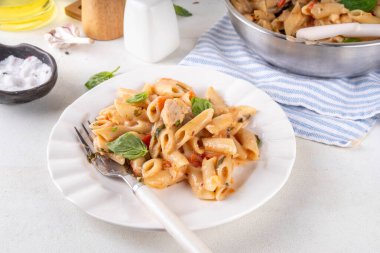 Son moda viral benimle tavuk makarnası evlen. Bir tencere yumuşak makarna ve kremalı ve peynirli sulu tavuk parçaları, sarımsaklı güneşte kurutulmuş domates sosu, nükteli fesleğen yaprağı, tabak ve demlikte.