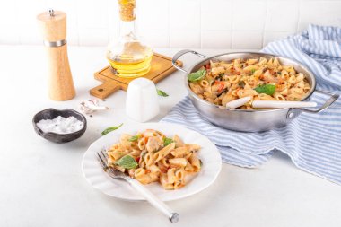 Son moda viral benimle tavuk makarnası evlen. Bir tencere yumuşak makarna ve kremalı ve peynirli sulu tavuk parçaları, sarımsaklı güneşte kurutulmuş domates sosu, nükteli fesleğen yaprağı, tabak ve demlikte.