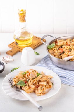 Son moda viral benimle tavuk makarnası evlen. Bir tencere yumuşak makarna ve kremalı ve peynirli sulu tavuk parçaları, sarımsaklı güneşte kurutulmuş domates sosu, nükteli fesleğen yaprağı, tabak ve demlikte.